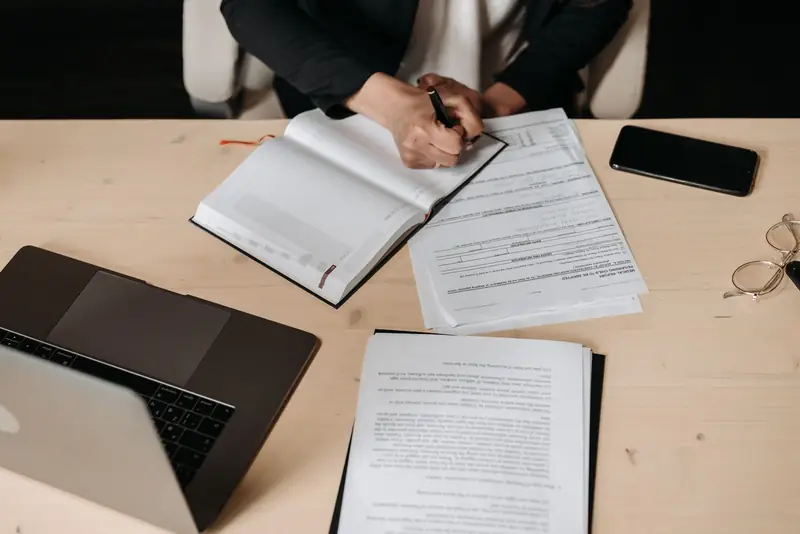 A person reviewing documents and writing notes at a desk